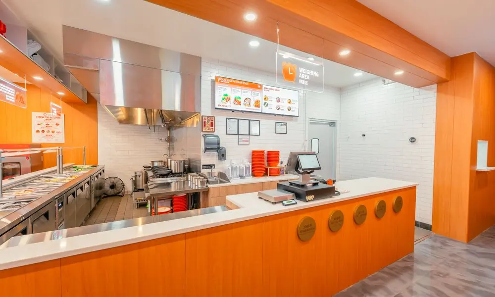 Order and weighing area with open kitchen, menu boards, and orange decor at YGF Malatang-Katy, a Chinese Restaurant in Katy