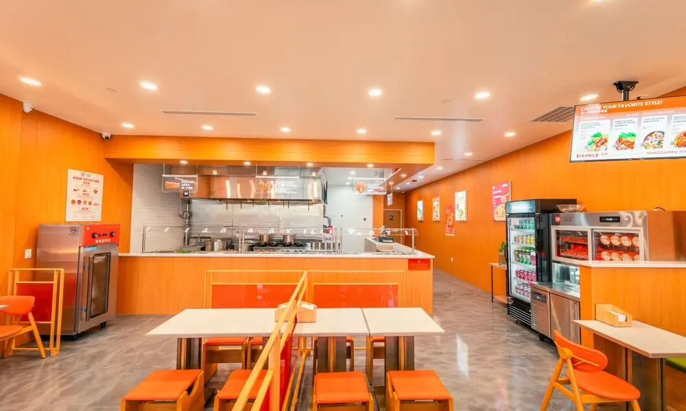 Bright restaurant interior with dining tables, orange seating, and beverage refrigerators at YGF Malatang-Katy, a Chinese Restaurant in Katy