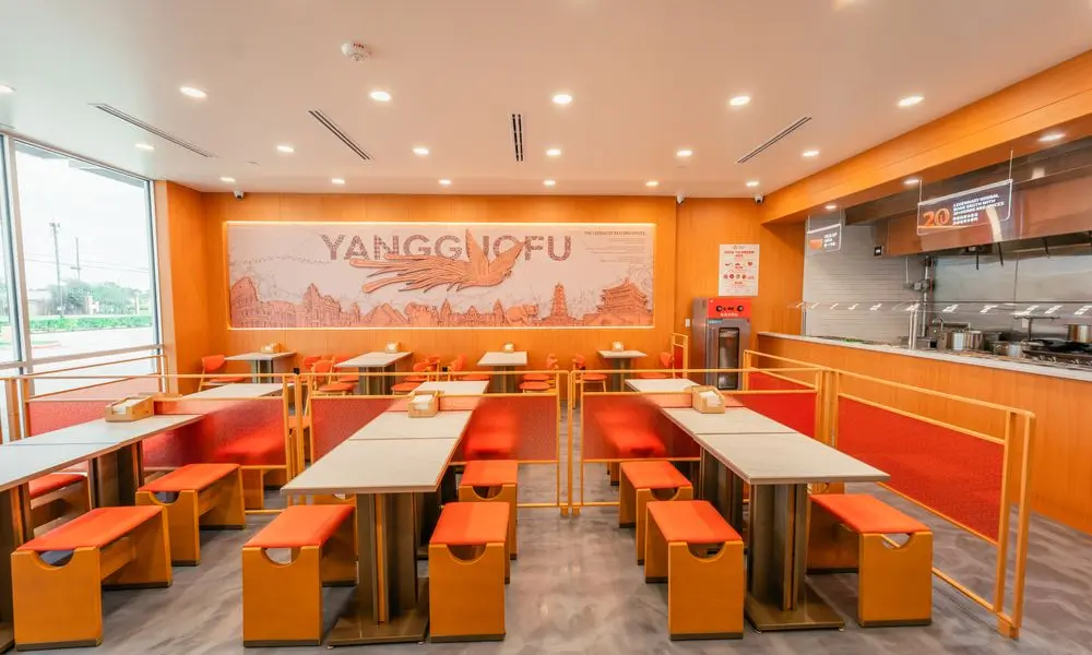 Dining area with large windows, "YANGGUOFU" wall art, and orange seating at YGF Malatang-Katy, a Chinese Restaurant in Katy