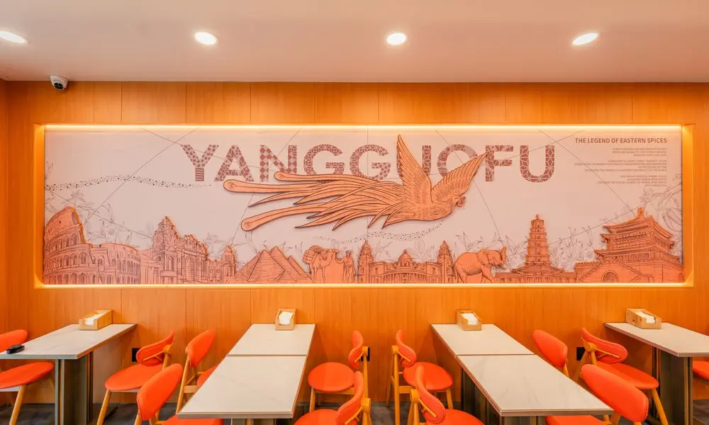 Wall art with "YANGGUOFU" and global landmarks, plus orange dining setup at YGF Malatang-Katy, a Chinese Restaurant in Katy